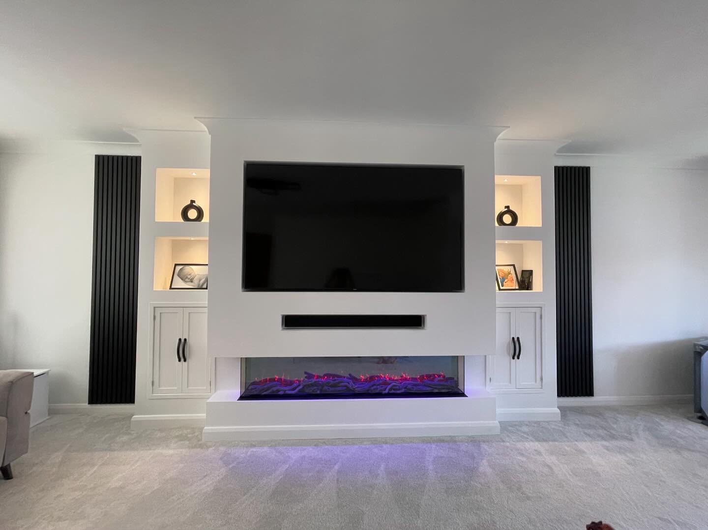 Finished white plastered media wall with electric fireplace, mounted TV and built-in storage